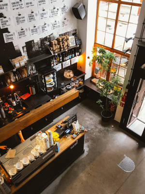現代咖啡店內部，設有木製櫃檯、黑色層架，以及靠近窗戶的盆栽植物。 — 咖啡美學 壁紙