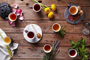 木桌上擺放著各式花草茶杯，搭配鮮花和香草。 — 茶園 壁紙