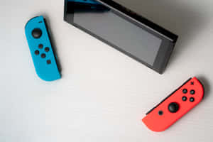 白色木桌上帶有紅色和藍色控制器的Nintendo Switch主機。 — MacBook Air M2 壁紙