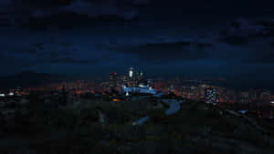 從山坡上俯瞰的夜景城市景觀，帶有發光的燈光和星空。 — 俠盜獵車手V 壁紙