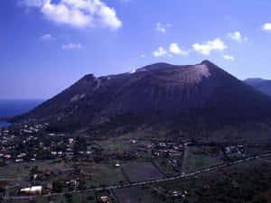 藍天白雲下，火山下方有一個沿海小鎮。 — 義大利 GIF 壁紙