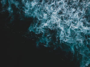 從空中俯瞰海浪破碎，白色泡沫與黑暗海水形成對比。 — 海軍藍 壁紙