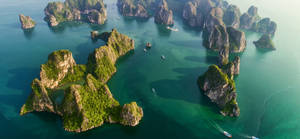 從空中俯瞰碧綠海水中鬱鬱蔥蔥的島嶼，有小船。 — 岩石 壁紙