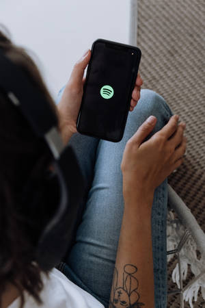 戴著耳機的人手持打開了Spotify應用程式的電話。 — Valorant iPhone 壁紙