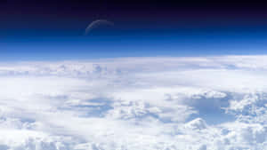 從蓬鬆的白雲上方俯瞰，藍天中有一彎新月 — 太空 壁紙