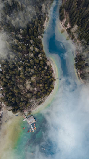 從高空俯瞰，一條霧氣瀰漫的碧綠河流蜿蜒穿過茂密的常綠森林，平靜的水面上有皮划艇愛好者。 — 編輯 壁紙