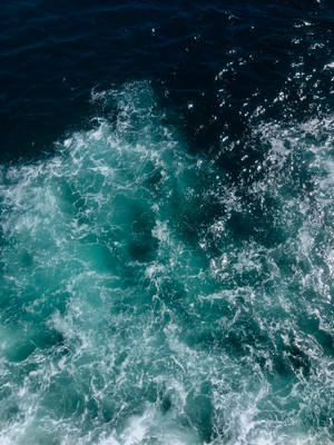 從上方觀看，綠松石色的海浪帶著白色泡沫撞擊深藍色海水。 — 水 壁紙