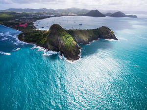 從高空俯瞰，碧綠的海浪拍打著綠色懸崖，遠處島嶼和沿海城鎮。 — 桌面 壁紙