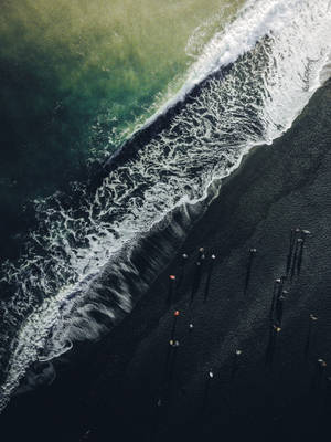 高空拍攝綠松石色海浪與黑色沙灘交匯，沙灘上有細小的人影在行走。 — 波浪 壁紙