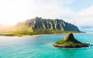 翠綠的山巒從碧綠的海水中升起，附近有一個小島。 — 日落 壁紙