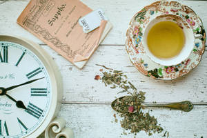 復古時鐘、茶杯和茶葉在質樸的木質表面上。 — 茶園 壁紙
