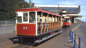 紅色復古電車37號在軌道上，背景有藍色護柱和現代建築。 — 1920x1080 壁紙