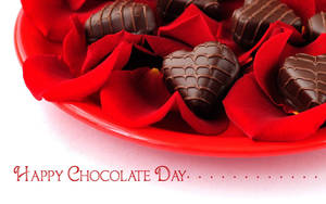 紅色玫瑰花瓣和心形巧克力放在紅色盤子上，並有「Happy Chocolate Day」字樣。 — 巧克力 壁紙
