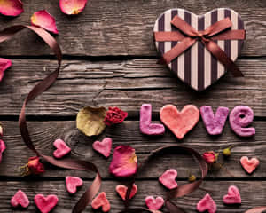 心形禮物盒和粉紅色黏土心形在木桌上拼出 love，並有玫瑰花瓣。 — 設計 壁紙