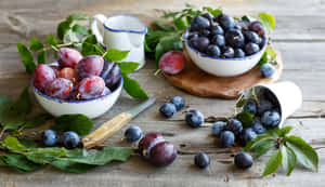 新鮮的李子放在碗裡，散落在木桌上，搭配樹葉。 — 柳橙 壁紙