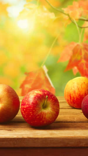 木桌上的新鮮紅蘋果，搭配秋葉和陽光。 — 柳橙 壁紙