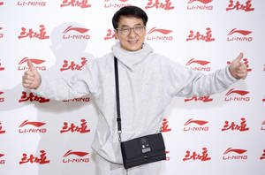 成龍在李寧活動中穿著灰色連帽衫和黑色包包，豎起兩個大拇指。 — 傑基·羅賓森 壁紙