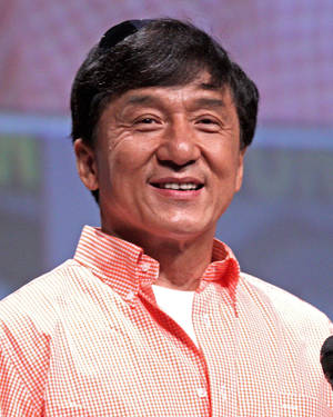 成龍在公開活動中身穿紅白格紋襯衫微笑。 — 粉紅色 壁紙