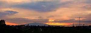 城市天際線在鮮豔的夕陽下呈現剪影，遠方有山。 — 夕陽天空 壁紙