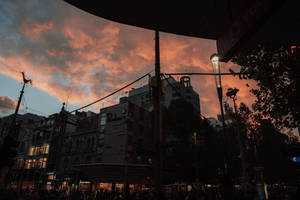 黃昏時分，繁忙城市街道上空戲劇性的橙色和粉紅色日落，建築物和雨傘形成剪影。 — 垃圾美學 壁紙
