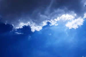 黑暗的暴風雲裂開，讓陽光穿過深藍色的天空。 — 藍天 壁紙