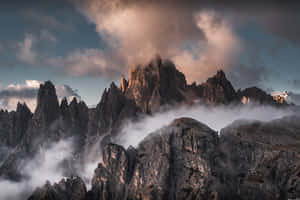 鋸齒狀山峰聳立於迷霧之上，金色的黎明之光穿透雲層。 — 免費 壁紙