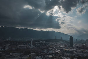 在戲劇性暴風雲下，陽光穿透雲層，照耀著山脈和城市景觀。 — 瓜達拉哈拉 壁紙