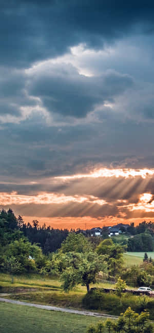 陽光穿過暴風雲，照耀在一個有樹木和房屋的綠色山谷上。 — 平靜 GIF 壁紙