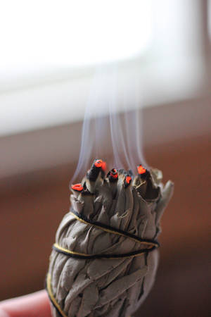 手持一根燃燒的鼠尾草煙燻棒，煙霧升起。 — 靈性動圖 壁紙