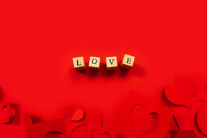 拼出LOVE的木塊放在紅色背景上，配有紙心。 — 我愛你這麼多 壁紙