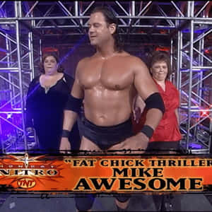 摔角手 Mike Awesome 在擂台上，身後有兩名女子，在舞台燈光下。 — 摔角 壁紙