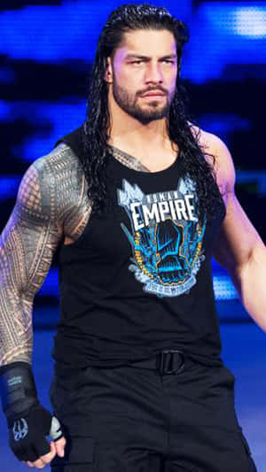 Roman Reigns 身穿黑色背心，帶有刺青和手套，在藍光下站在舞台上。 — 羅曼·雷恩斯 壁紙