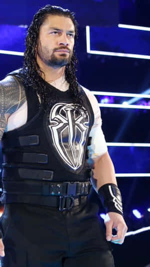 摔角手 Roman Reigns 身穿帶有白色標誌的黑色背心，站在舞台燈光下。 — 羅曼·雷恩斯 壁紙