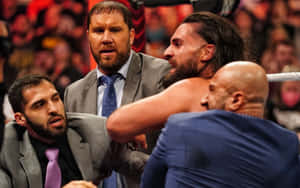 身穿西裝的摔角手和經理人在明亮的摔角擂台上打鬥。 — WWE GIF 壁紙