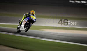 摩托車手在夜間賽道上比賽，帶有 '46 Rossi' 浮水印。 — 賽車 壁紙