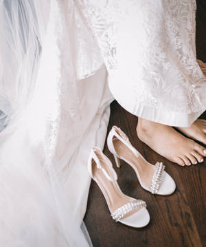 木地板上蕾絲婚紗旁邊的新娘赤腳和白色珠飾高跟鞋。 — 婚紗 壁紙