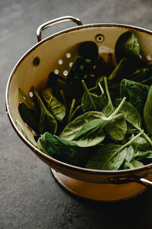 深色石檯面上的銅濾網中的新鮮菠菜 — 黑色五葉草 壁紙