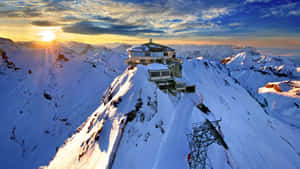 日出照耀白雪覆蓋的山峰，設有現代天文台及滑雪纜車設施。 — 瑞士 壁紙