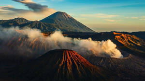 日出時噴出蒸氣的火山山峰，金色光芒照耀在崎嶇的地形上。 — 惠普筆電 壁紙