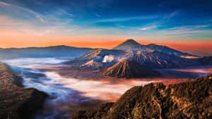 日出時分的火山山脈，薄霧流過山谷，山峰在溫暖的橙色和涼爽的藍色調中閃耀。 — 漂亮的桌面 壁紙
