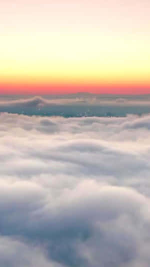 日出時雲層上方，橙色、粉紅色和黃色的天空，遠處的城市燈光 — 手機 壁紙