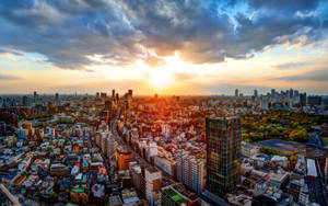夕陽映照在密集的城市，高樓大廈林立，金色光芒穿透雲層。 — 美學 Mac 壁紙