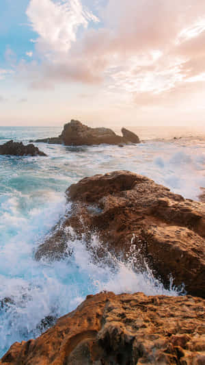 日落時分，海浪拍打著崎嶇的海岸岩石，在充滿活力的藍綠色海洋中。 — 高對比 壁紙