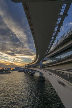 日落時分，水面上方的曲線橋，背景為城市天際線。 — 2:3 壁紙