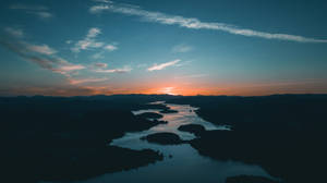 蜿蜒河流上的日落，暗色山丘形成剪影。 — 夕陽天空 壁紙