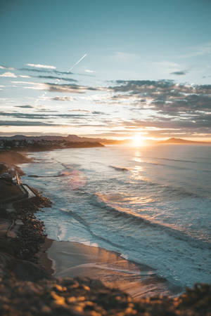 海岸日落，波浪拍打岸邊，遠山沐浴在金色光線中。 — 小米平板 9 Pro Max 壁紙