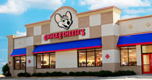 陽光普照的天空下，Chuck E Cheese's 餐廳配有吉祥物和藍色遮陽篷。 — 查克芝士 壁紙