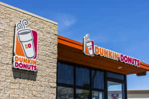 藍天下帶有橙色招牌和石質外牆的Dunkin' Donuts店舖。