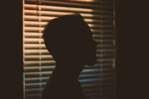 男子剪影望向窗外，百葉窗投射出光條。 — 暗色 壁紙