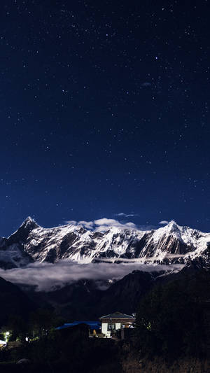 星空夜幕下的積雪山峰，山谷中亮燈的房子。 — 美麗的夜晚 壁紙